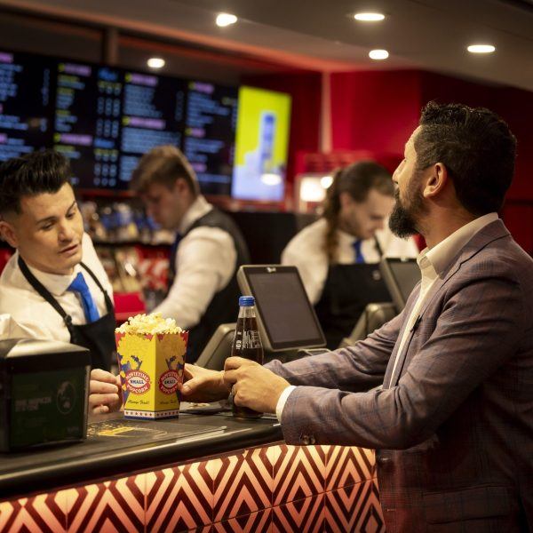 A Customer Exprience Team Member serves a man a soft drink and popcorn from the Riverside Theatres bar.